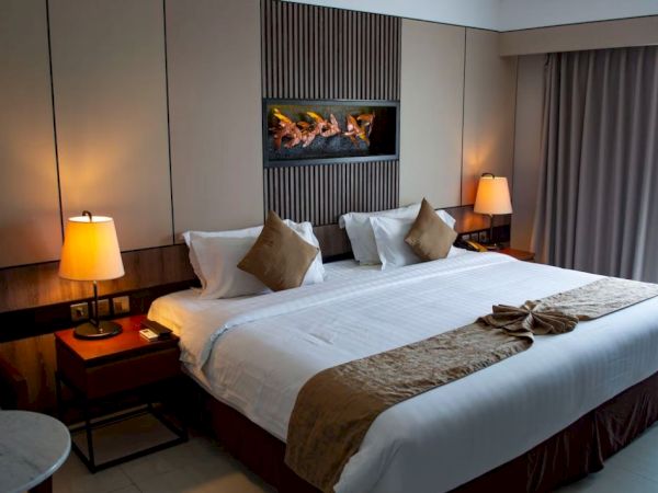 A hotel room with a large bed, decorative pillows, lamps on side tables, wall art, and curtains.