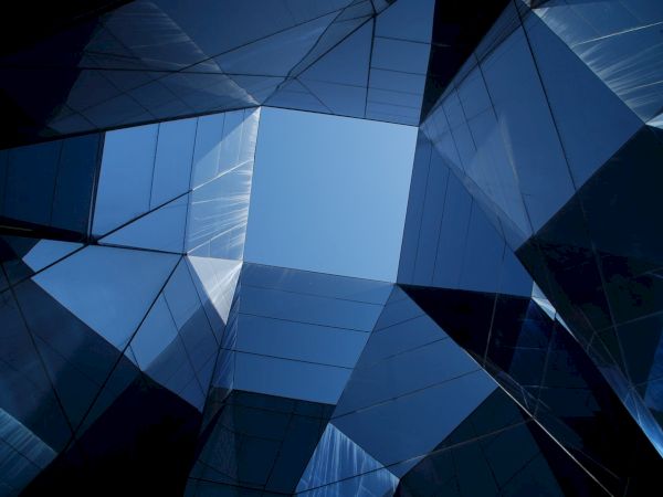 Abstract view of reflective glass skyscrapers forming a geometric pattern, showcasing a patch of blue sky at the center.