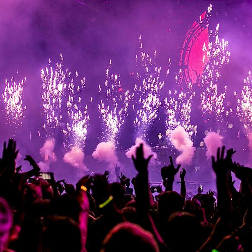 A vibrant concert scene with fireworks and cheering crowd, surrounded by pink and purple lights in an electrifying atmosphere.