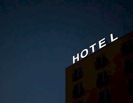 The image shows a building with a partially lit sign that reads "HOTEL," with the "L" illuminated against a dark sky.