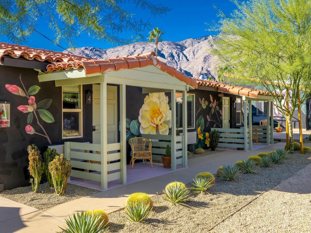 A colorful building with floral murals, red-tiled roof, and a desert landscape. There's a mountain in the background under a clear blue sky.