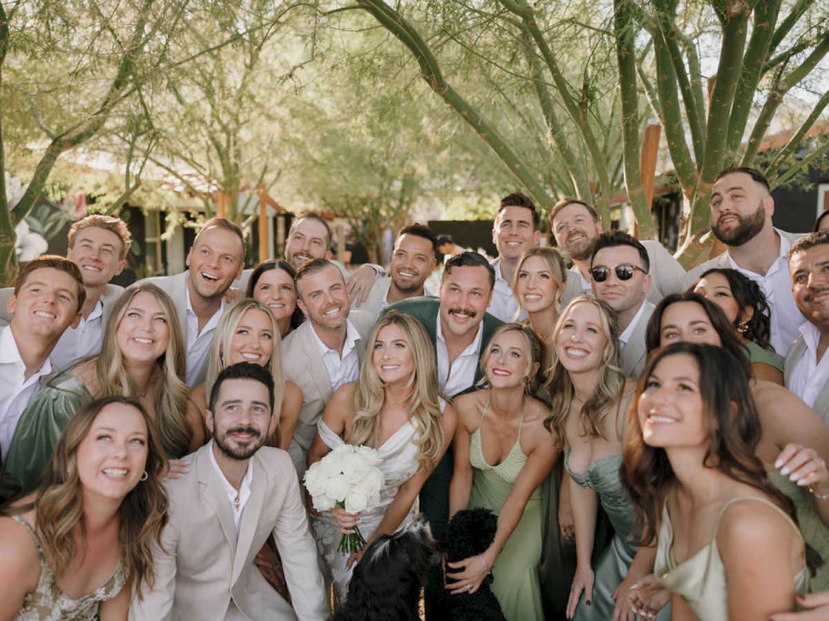 A group of people, dressed formally, smiling and gathered outdoors under trees, possibly celebrating or attending a special event.