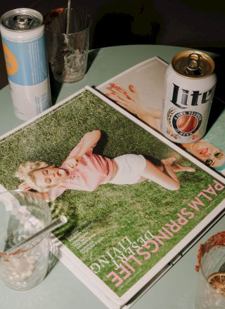 Magazines, a can of beer, a highball can, and glasses on a table.