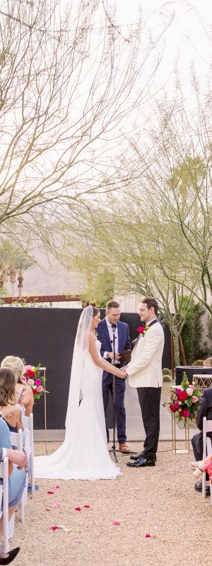 A couple getting married outdoors with guests seated, surrounded by trees and light decor in a warm setting.