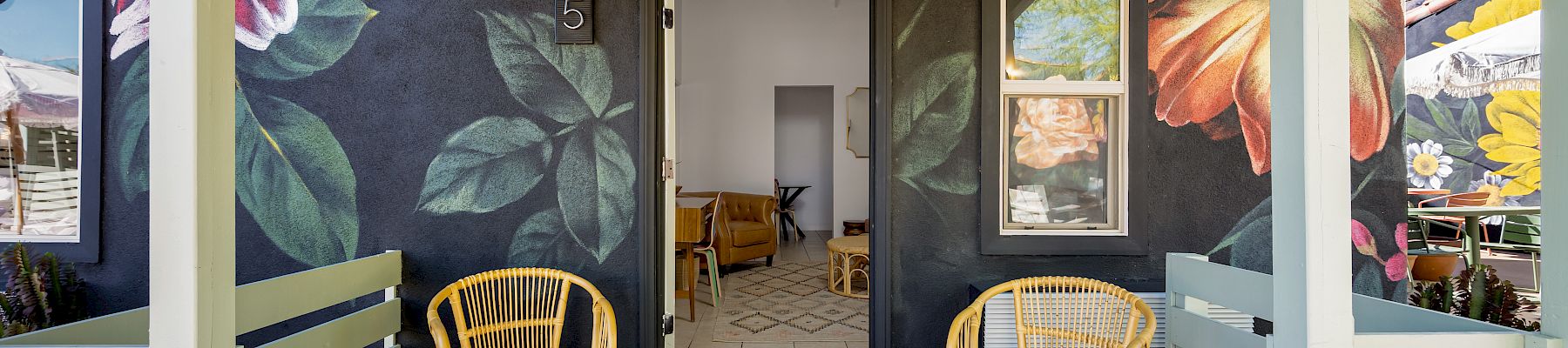 A porch with two yellow chairs, floral murals on walls, and an open door leading inside.