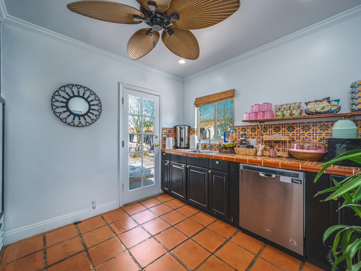 A kitchen with terracotta tiles, dark cabinets, stainless appliances, a ceiling fan, a decorative clock, and a view through the glass door.