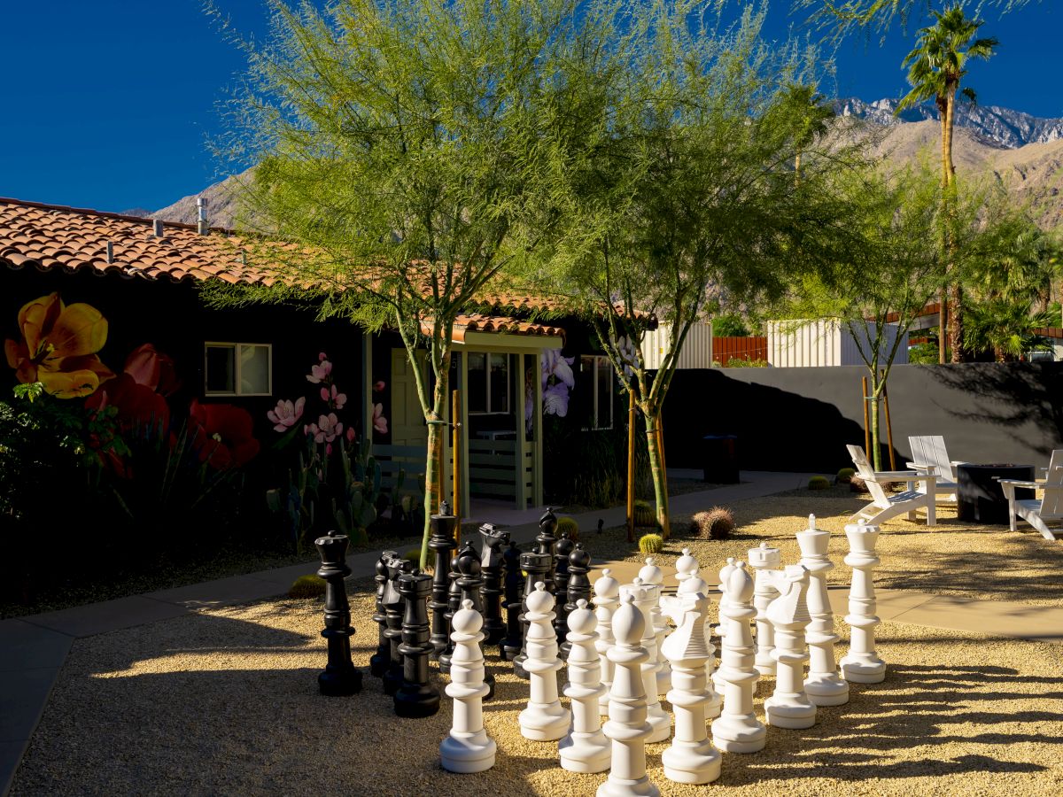 An outdoor area features a large chess set, trees, a mural, and mountains in the background.