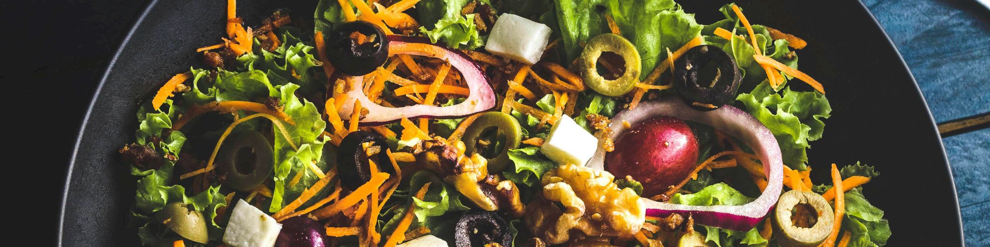 A fresh salad with lettuce, onions, olives, and walnuts on a plate, alongside a glass of orange juice and orange slices.