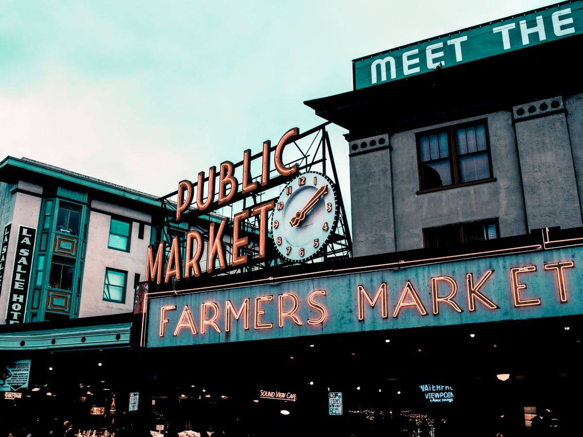 The image shows a vintage-style neon sign that reads "Public Market" and "Farmers Market," with a clock in the center.
